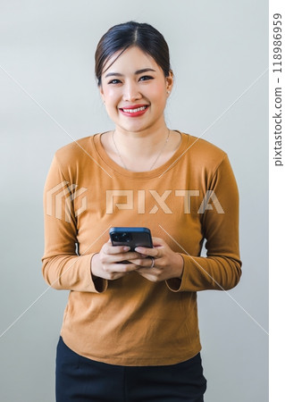 Confident asian woman with friendly smile stands with hand holding smartphone isolated on white background. 118986959