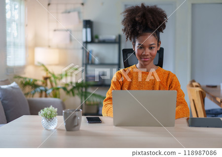 Young African American woman smiling while engaged in virtual meeting at home. 118987086