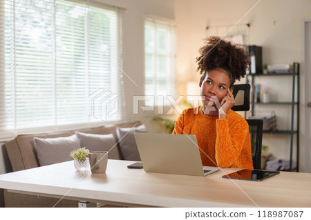 Young black woman in cozy sweater concentrating on laptop at home office during daytime. 118987087