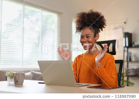 Young African American woman smiling while engaged in virtual meeting at home. 118987090