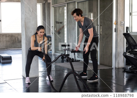 Strong Asian woman doing battle rope exercise with personal trainer 118988798