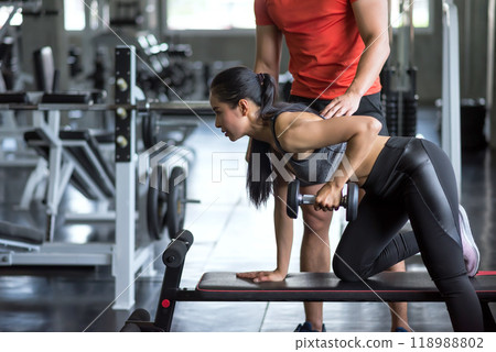 Asian woman doing dumbbell exercise with gym personal trainer 118988802