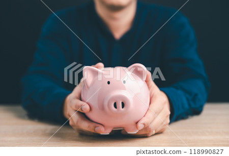 Man hand holding piggy bank on wood table with black background. The concept of saving money and financial investment Man hand holding piggy bank on wood table with black background. The concept of saving money and financial investment 118990827