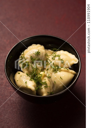 A bowl of potato dumplings with butter and dill on a burgundy background 118991904