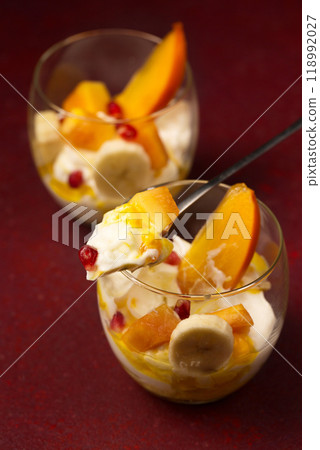 Delicious dessert with tropical fruits in transparent glasses on a burgundy background 118992027