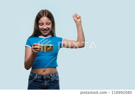 Girl happily cheering while using smartphone, celebrating success Girl happily cheering while using smartphone, celebrating success 118992080