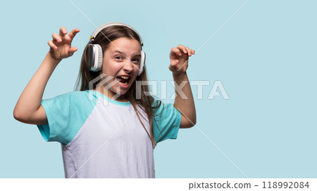 Girl making scary face with hands raised while wearing headphones. 118992084