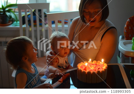 Young mother with two children blows out candles on birthday cake Young mother with two children blows out candles on birthday cake 118993305