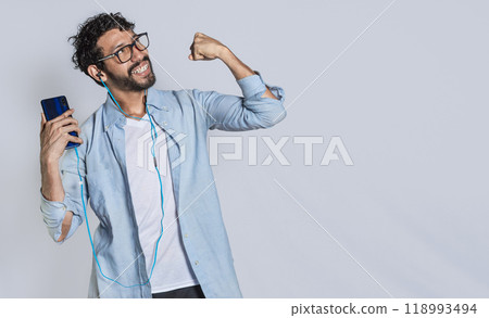 Happy handsome man with headphones holding a cell phone and celebrating, Happy person using his smartphone and celebrating victory isolated Happy handsome man with headphones holding a cell phone and celebrating, Happy person using his smartphone and celebrating victory isolated 118993494