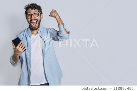 Excited man winning a prize from his cellphone. Excited handsome man looking at smartphone celebrating something. Happy person holding a smartphone and celebrating 118993495