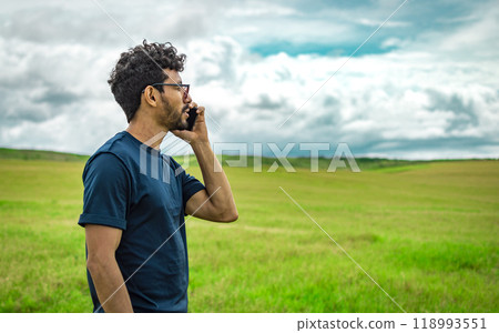 Man on the road talking on the phone, person in the field calling on the phone, young man talking on the phone in the field looking to the side. Handsome man calling on the phone in the field Man on the road talking on the phone, person in the field calling on the phone, young man talking on the phone in the field looking to the side. Handsome man calling on the phone in the field 118993551