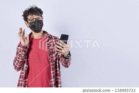Teen guy with mask making video call from his cell phone, Man with surgical mask making video call isolated, face mask video call concept Teen guy with mask making video call from his cell phone, Man with surgical mask making video call isolated, face mask video call concept 118993722