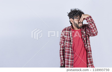 Portrait of man holding his nose looking at camera, people holding his nose with unpleasant smell expression, young man with bad smell expression holding his nose. 118993730