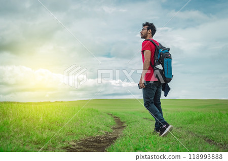 Side view of backpacking man on a beautiful road in the countryside. Young explorer man walking in a green field, Backpacker man walking in a beautiful field. Side view of backpacking man on a beautiful road in the countryside. Young explorer man walking in a green field, Backpacker man walking in a beautiful field. 118993888