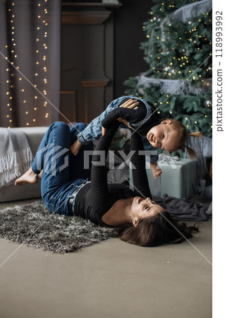 Mother and child playing happily by Christmas tree indoors Mother and child playing happily by Christmas tree indoors 118993992
