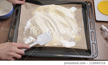 The process of making dough. Woman mixes powdered sugar and almond flour with silicone spatula on tray in kitchen. Baking macarons at home. Hands close-up. The process of making dough. Woman mixes powdered sugar and almond flour with silicone spatula on tray in kitchen. Baking macarons at home. Hands close-up. 118994316
