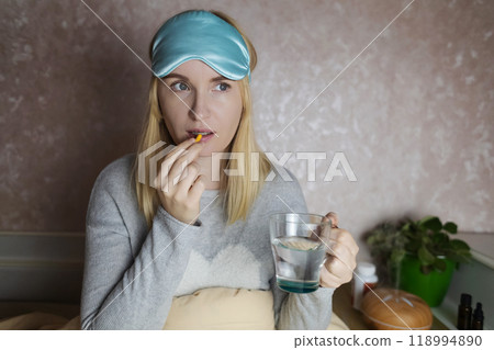 A woman cannot fall asleep and wants to drink a capsule with melatonin, a sleeping pill. Manifestations of jitlag or insomnia. Regulation of biological rhythms 118994890