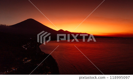 Aerial view panorama of coastline with silhouette of volcano and sunset with quiet sea in Bali. Aerial view panorama of coastline with silhouette of volcano and sunset with quiet sea in Bali. 118995097