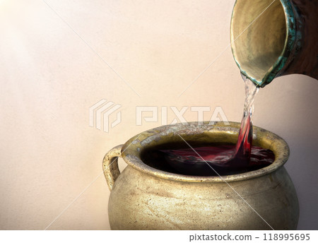 A hand holds a clay jar and pours water A hand holds a clay jar and pours water 118995695