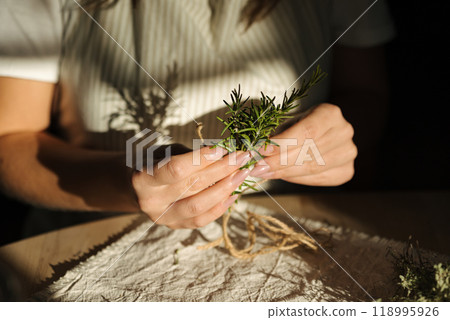 Female hand uses natural twine to tie rosemary sprigs. Preparing fresh herbs for drying and spice use Female hand uses natural twine to tie rosemary sprigs. Preparing fresh herbs for drying and spice use 118995926