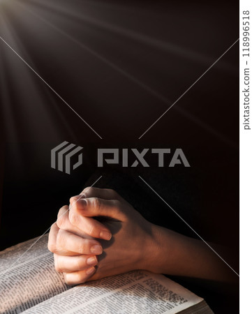 Hands clasped in prayer near an open book 118996518