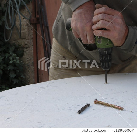 male hands firmly holding green screwdriver and pressing screw fastener into white surface of round table top, fixing wooden top on garden table with hand tool male hands firmly holding green screwdriver and pressing screw fastener into white surface of round table top, fixing wooden top on garden table with hand tool 118996807