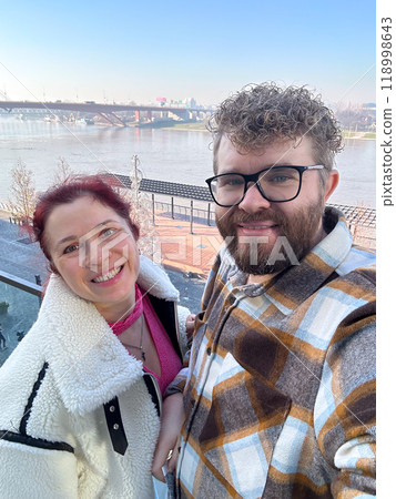 Man and woman taking selfie in cold time outdoor. Couple enjoying a beautiful day by the river with a breathtaking view. Moment of connection and joy together 118998643