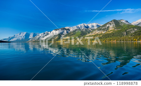 Banff National Park Lake Minnewanka autumn landscape. Alberta, Canada. Majestic mountains, forests in yellow green color against blue sky reflected on the water. Beautiful natural scenery. 118998878