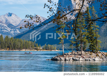 Banff National Park Lake Minnewanka autumn landscape. A rock island with fir trees. Majestic mountains, forests against blue sky. Alberta, Canada. Canadian Rockies beautiful natural scenery. Banff National Park Lake Minnewanka autumn landscape. A rock island with fir trees. Majestic mountains, forests against blue sky. Alberta, Canada. Canadian Rockies beautiful natural scenery. 118998882