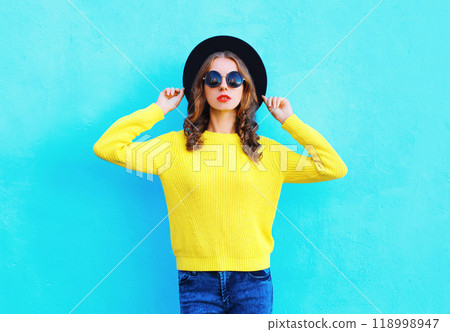 Fashion beautiful woman wearing a black hat, yellow knitted sweater on colorful blue background 118998947
