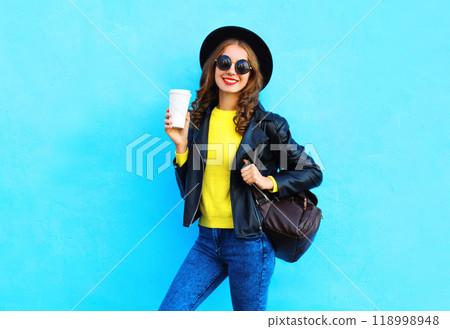 Fashion happy smiling woman with coffee cup in black rock style clothes on colorful blue background Fashion happy smiling woman with coffee cup in black rock style clothes on colorful blue background 118998948