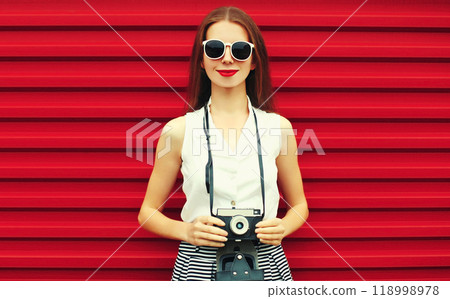 Summer portrait of young woman photographer with vintage film camera on colorful red background 118998978