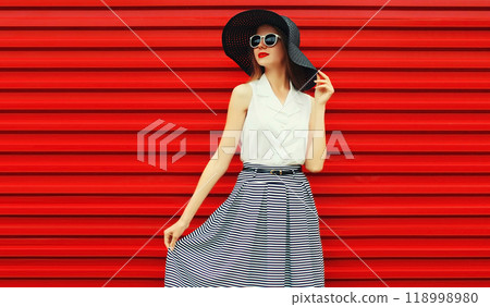 Portrait of stylish young woman model posing wearing black summer straw round hat on red background 118998980