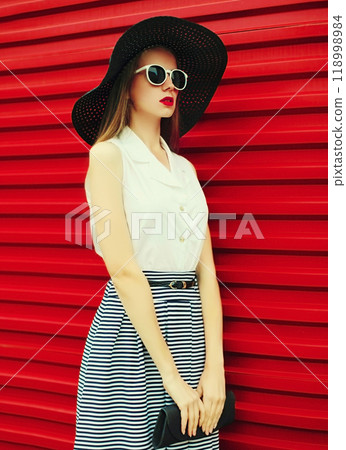Portrait of stylish young woman model posing wearing summer round hat, handbag on red background Portrait of stylish young woman model posing wearing summer round hat, handbag on red background 118998984