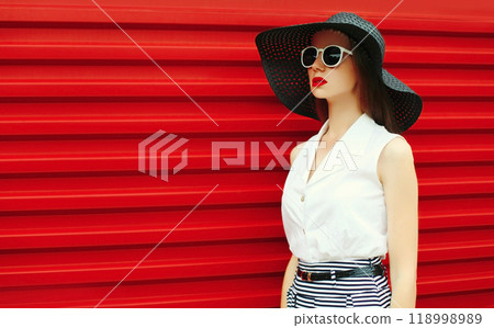 Portrait of stylish young woman model posing wearing black summer straw round hat on red background 118998989
