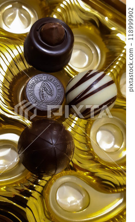 Beautiful chocolate candies. Candies of different shapes in golden packaging, illuminated by a beam of light. 118999902