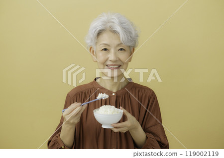 A gray-haired senior woman holding a bowl of rice and chopsticks A gray-haired senior woman holding a bowl of rice and chopsticks 119002119