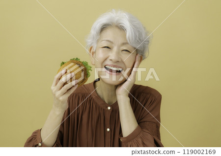 White-haired senior woman holding a cutlet burger 119002169