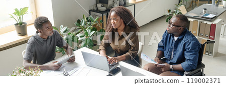 Website banner of young African American team of developers sitting at white table with laptops and having business meeting 119002371
