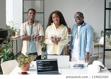 Portrait of African American young team of talented programmers standing next to work desk and smiling while looking at camera 119002400