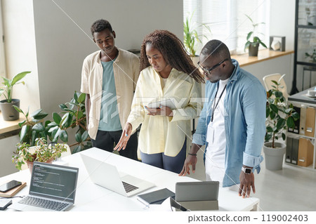 African American female teamlead with tablet in hands discussing work plan together with his subordinates 119002403