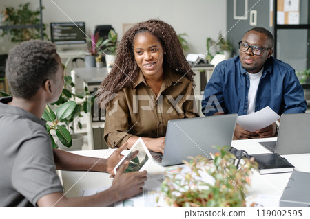 Young and beautiful African American programmer smiling widely while looking at her male colleague with tablet in hands 119002595