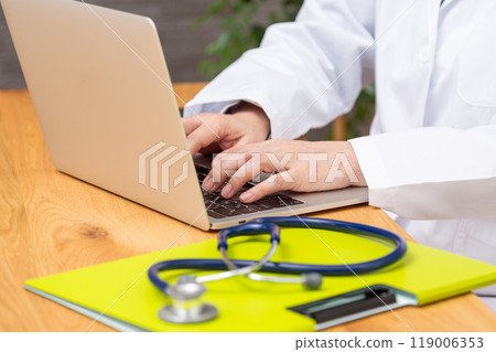 A senior female doctor in a white coat doing desk work 119006353