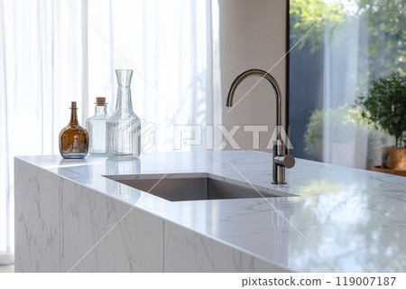A sleek modern kitchen with a marble countertop, metal faucet, and glass bottles lit by natural light A sleek modern kitchen with a marble countertop, metal faucet, and glass bottles lit by natural light 119007187