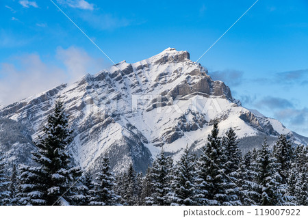 Close up snow-covered Cascade Mountain with snowy forest over blue sky and white clouds in winter sunny day. Banff National Park beautiful landscape. Canadian Rockies, Alberta, Canada. 119007922