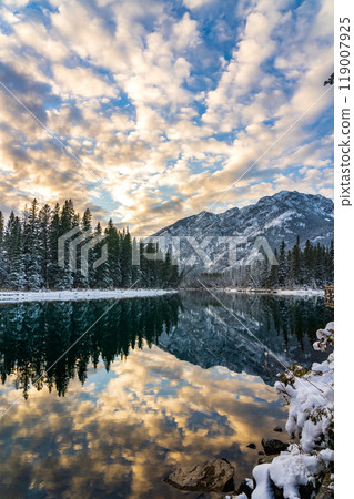 Banff National Park beautiful natural scenery in winter sunset time. Mount Norquay with colourful clouds reflected on Bow River like a mirror. Town of Banff, Canadian Rockies. Banff National Park beautiful natural scenery in winter sunset time. Mount Norquay with colourful clouds reflected on Bow River like a mirror. Town of Banff, Canadian Rockies. 119007925
