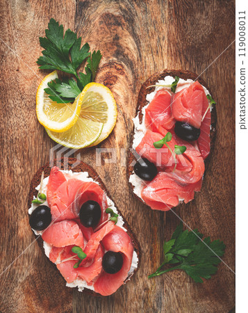 sandwiches with cream cheese, chum salmon, cold smoked, grain bread, on a cutting board, top view, breakfast, lemon and parsley, no people, 119008011