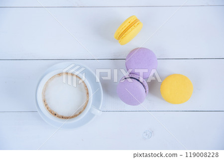 Sweet delicious violet and yellow macarons and cup of latte or americano on white wooden background. 119008228