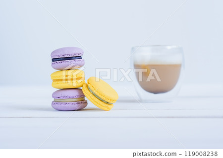 Tasty violet and yellow macarons and cup of latte on white wooden background. 119008238