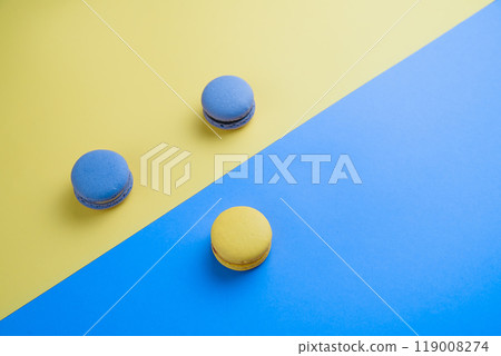 Sweet tasty blue and yellow french macaron cakes on yellow and blue background. Sweet tasty blue and yellow french macaron cakes on yellow and blue background. 119008274